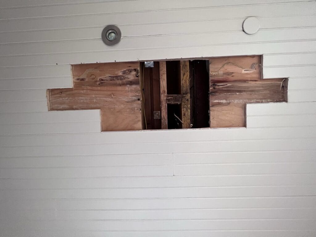 Ceiling with a rectangular hole exposing wooden beams.